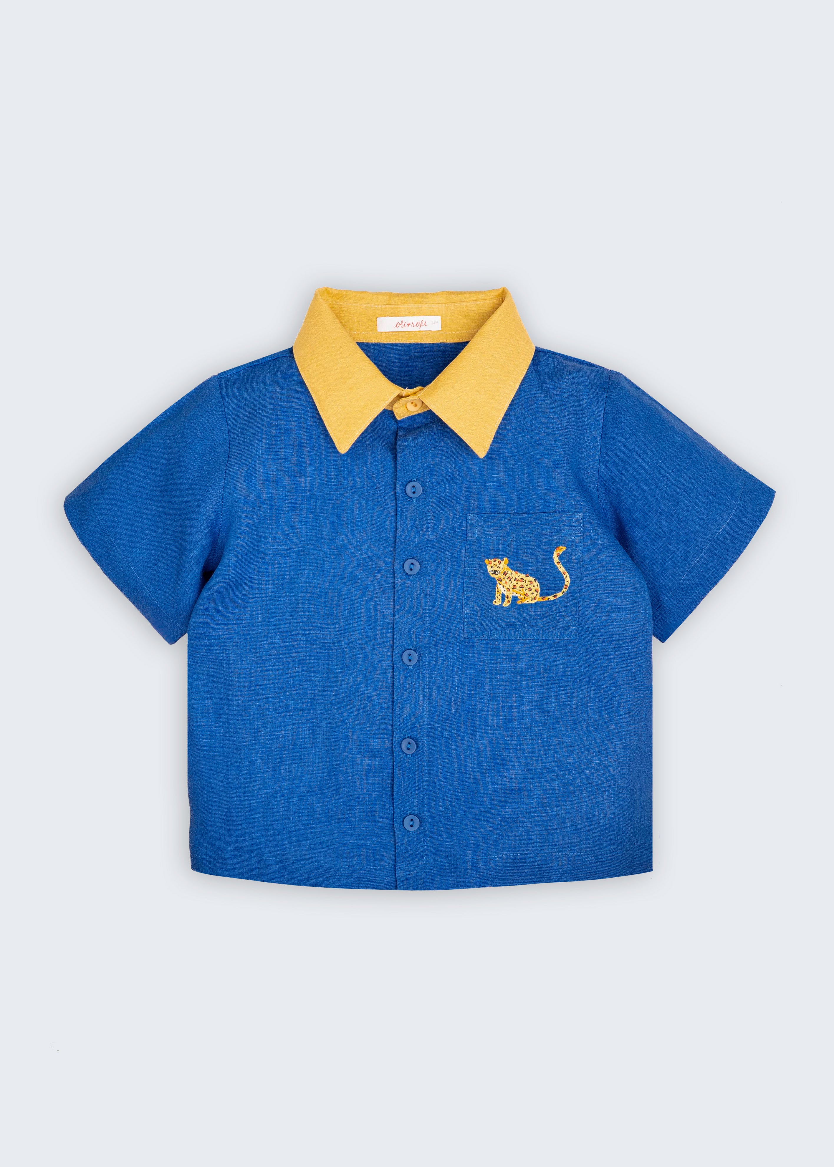 Camisa infantil Tom em linho puro azul com gola amarela e bordado à mão de onça no bolso frontal, vista de frente.