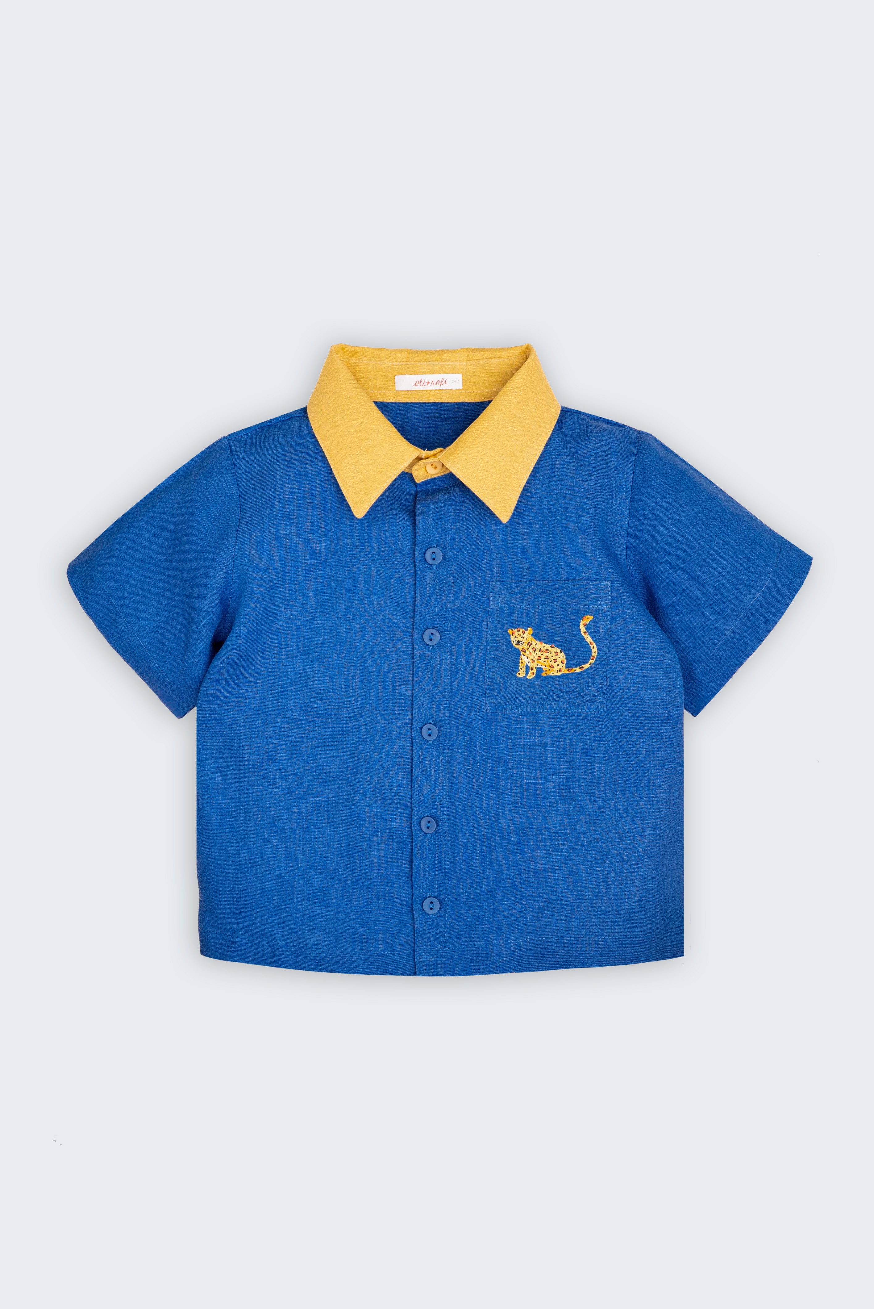 Camisa infantil Tom em linho puro azul com gola amarela e bordado à mão de onça no bolso frontal, vista de frente.