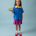 Menina usando camisa infantil azul e amarela em linho puro com bordado de onça, combinada com saia roxa