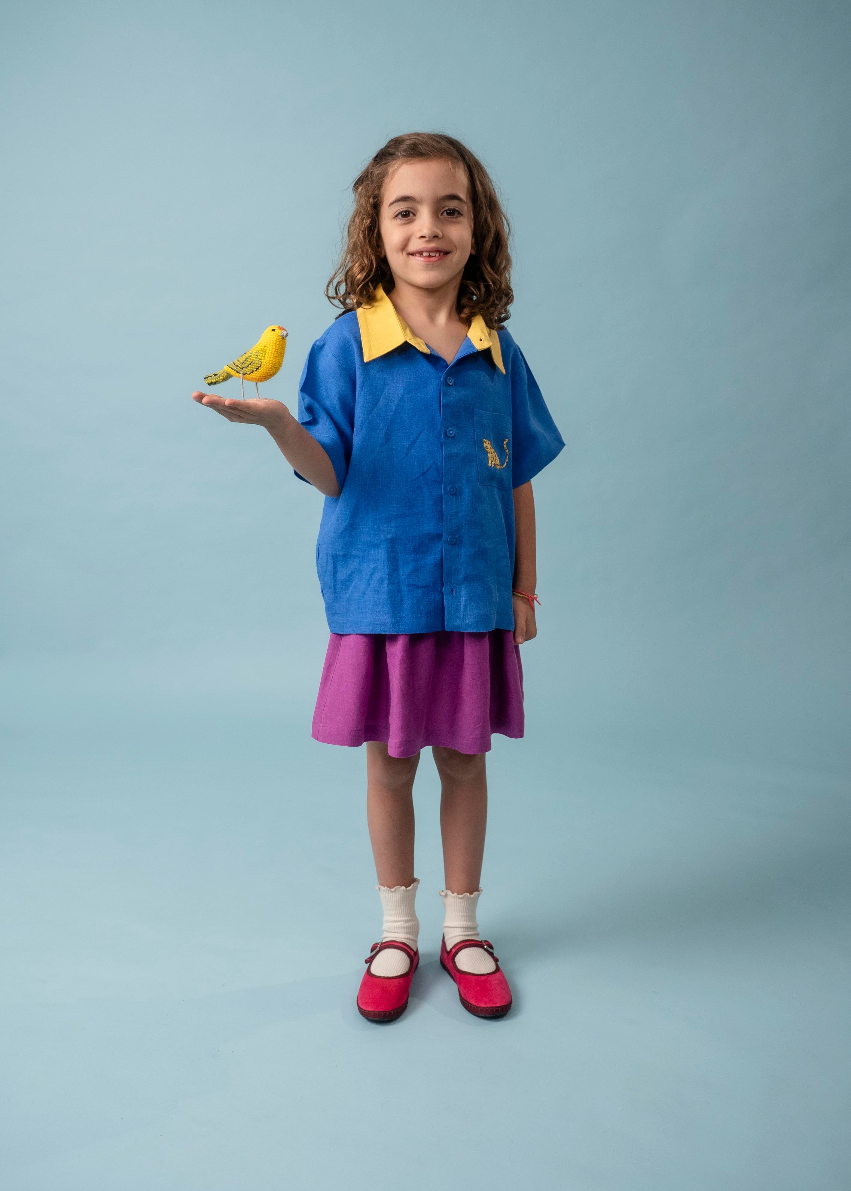 Menina usando camisa infantil azul e amarela em linho puro com bordado de onça, combinada com saia roxa