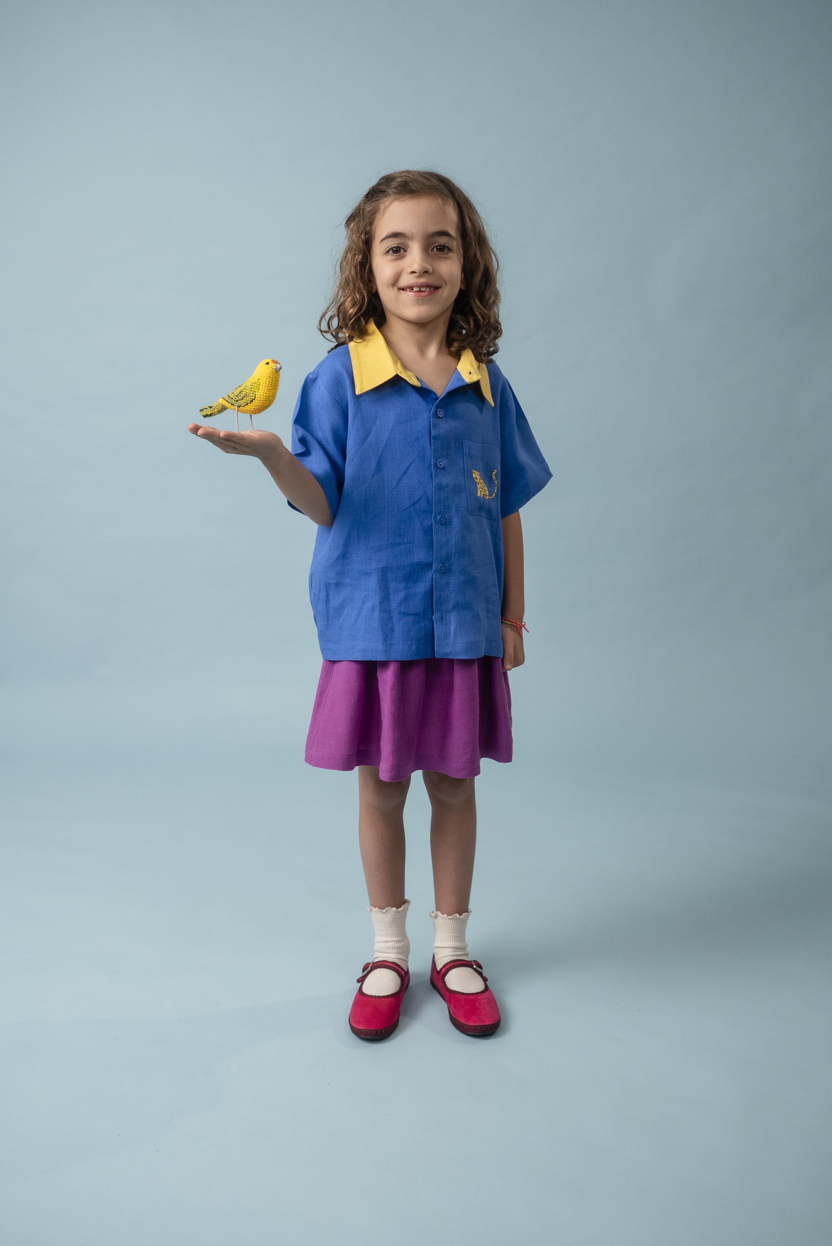Menina usando camisa infantil azul e amarela em linho puro com bordado de onça, combinada com saia roxa
