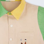 Camisa infantil em linho puro bege, verde e amarelo com bordado à mão de jogador de futebol no bolso, vista em detalhe