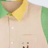 Camisa infantil em linho puro bege, verde e amarelo com bordado à mão de jogador de futebol no bolso, vista em detalhe