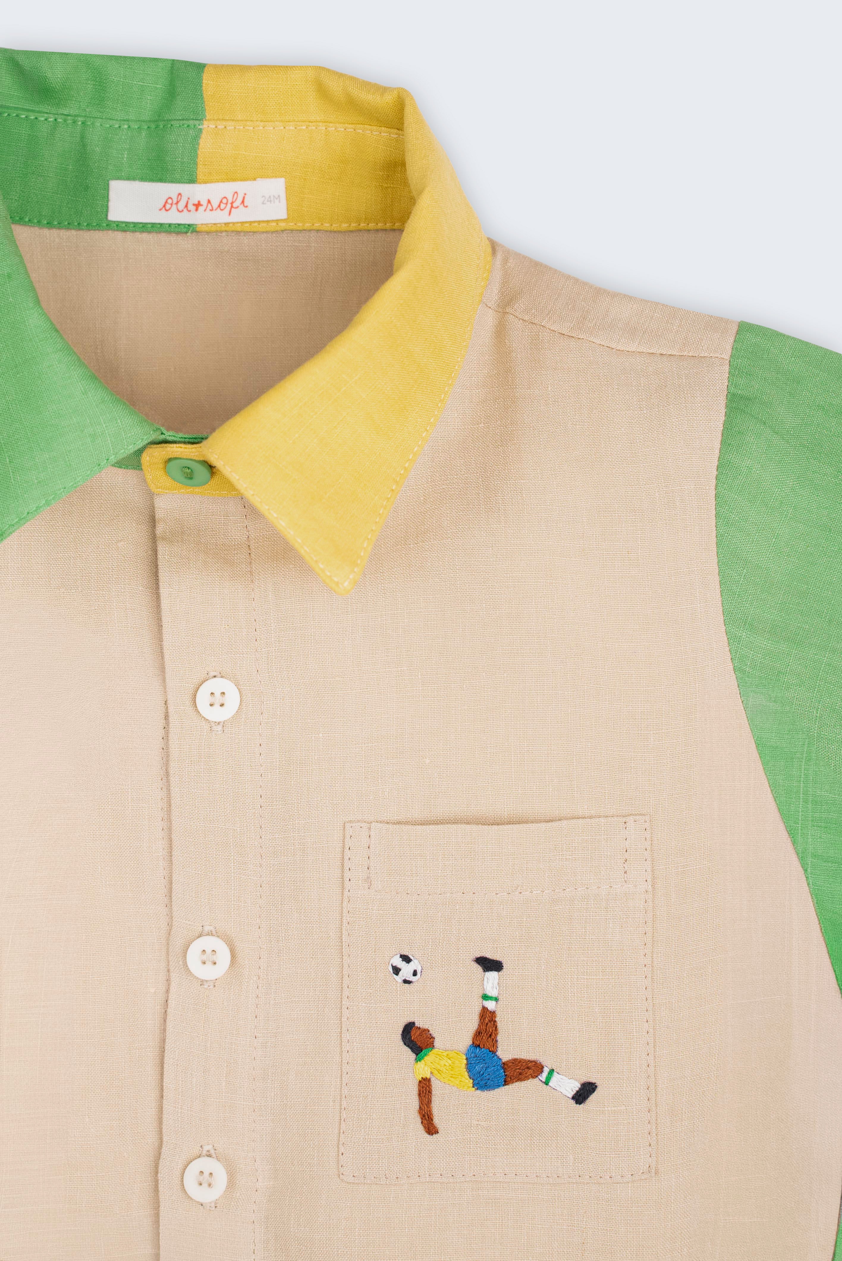 Camisa infantil em linho puro bege, verde e amarelo com bordado à mão de jogador de futebol no bolso, vista em detalhe