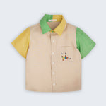 Camisa infantil em linho puro bege com mangas verde e amarela, gola bicolor e bordado de jogador de futebol no bolso, vista de frente
