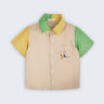 Camisa infantil em linho puro bege com mangas verde e amarela, gola bicolor e bordado de jogador de futebol no bolso, vista de frente