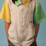 Menina usando camisa infantil de linho bege, verde e amarelo com bordado de jogador de futebol no bolso