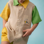 Menino usando camisa infantil em linho bege com mangas verde e amarela e bordado à mão de jogador no bolso