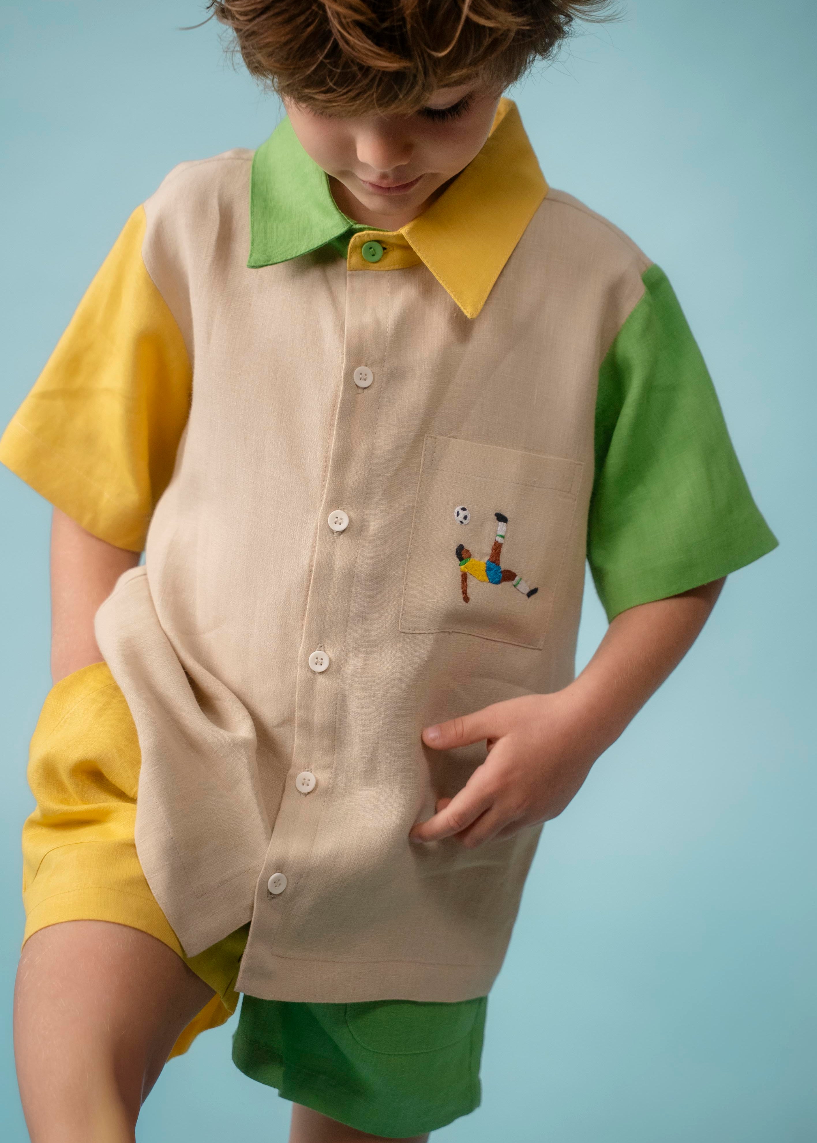 Menino usando camisa infantil em linho bege com mangas verde e amarela e bordado à mão de jogador no bolso