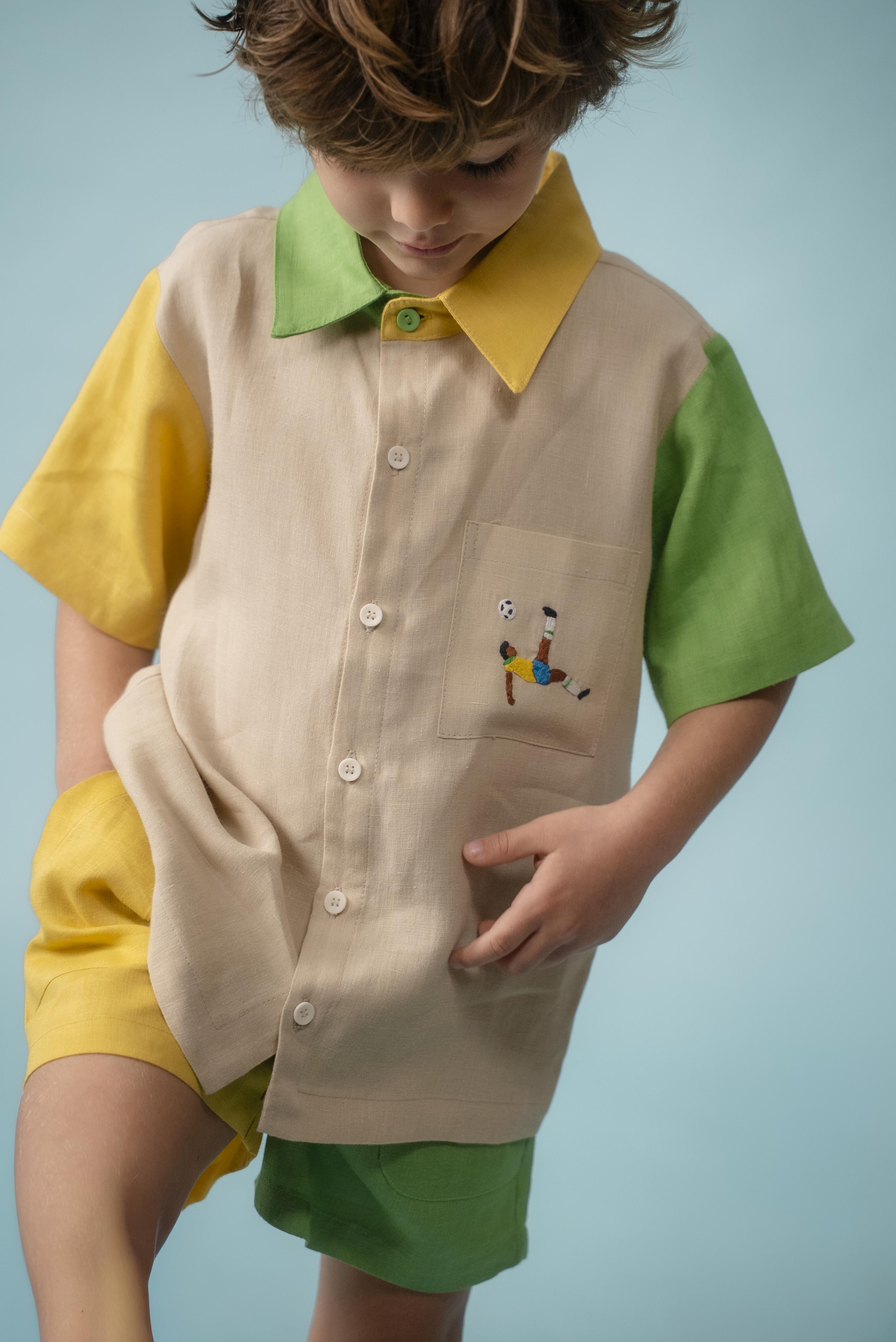 Menino usando camisa infantil em linho bege com mangas verde e amarela e bordado à mão de jogador no bolso