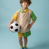 Menino usando Camisa Tom em linho puro com bordado de jogador de futebol, combinada com shorts bicolor verde e amarelo