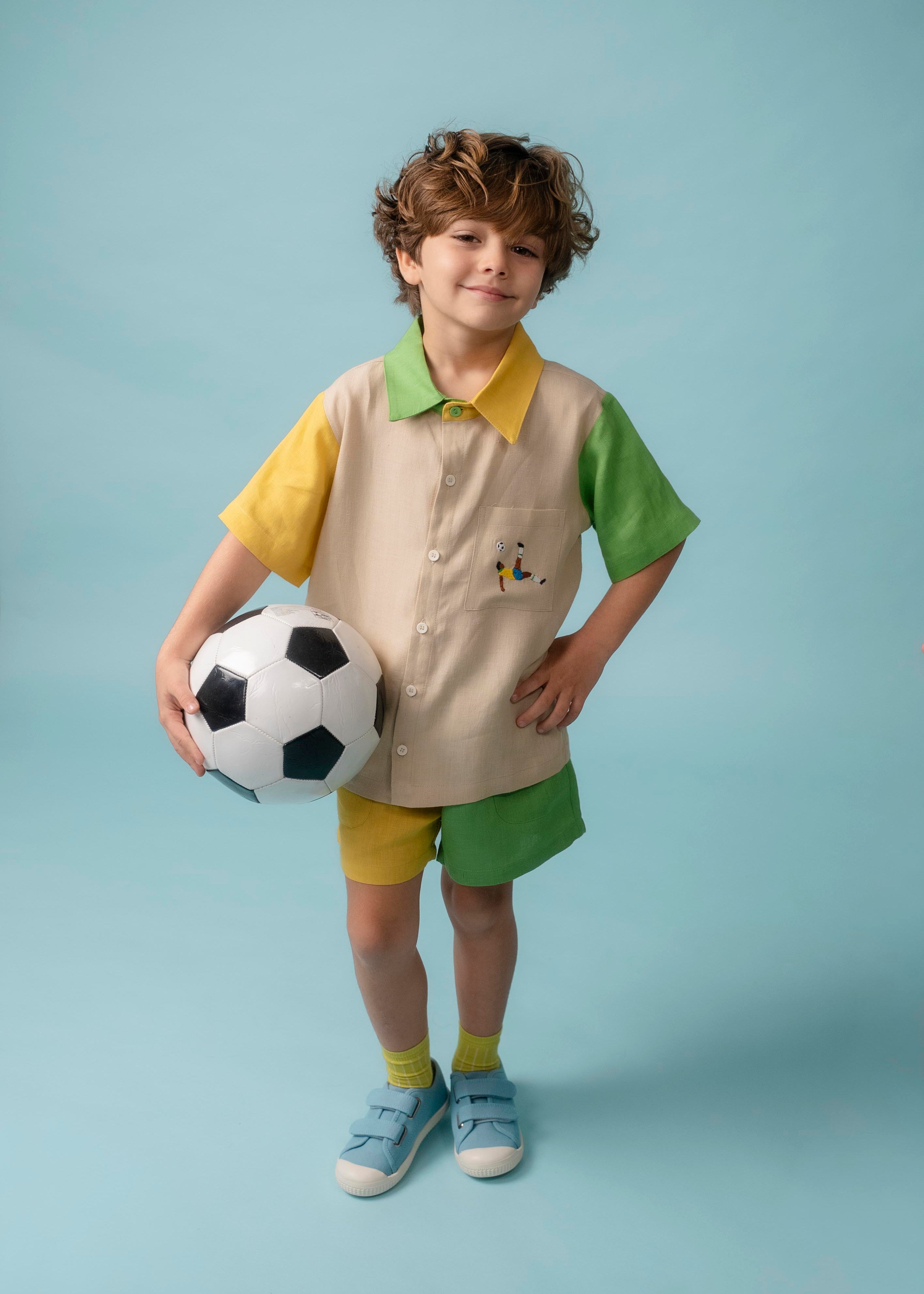 Menino usando Camisa Tom em linho puro com bordado de jogador de futebol, combinada com shorts bicolor verde e amarelo