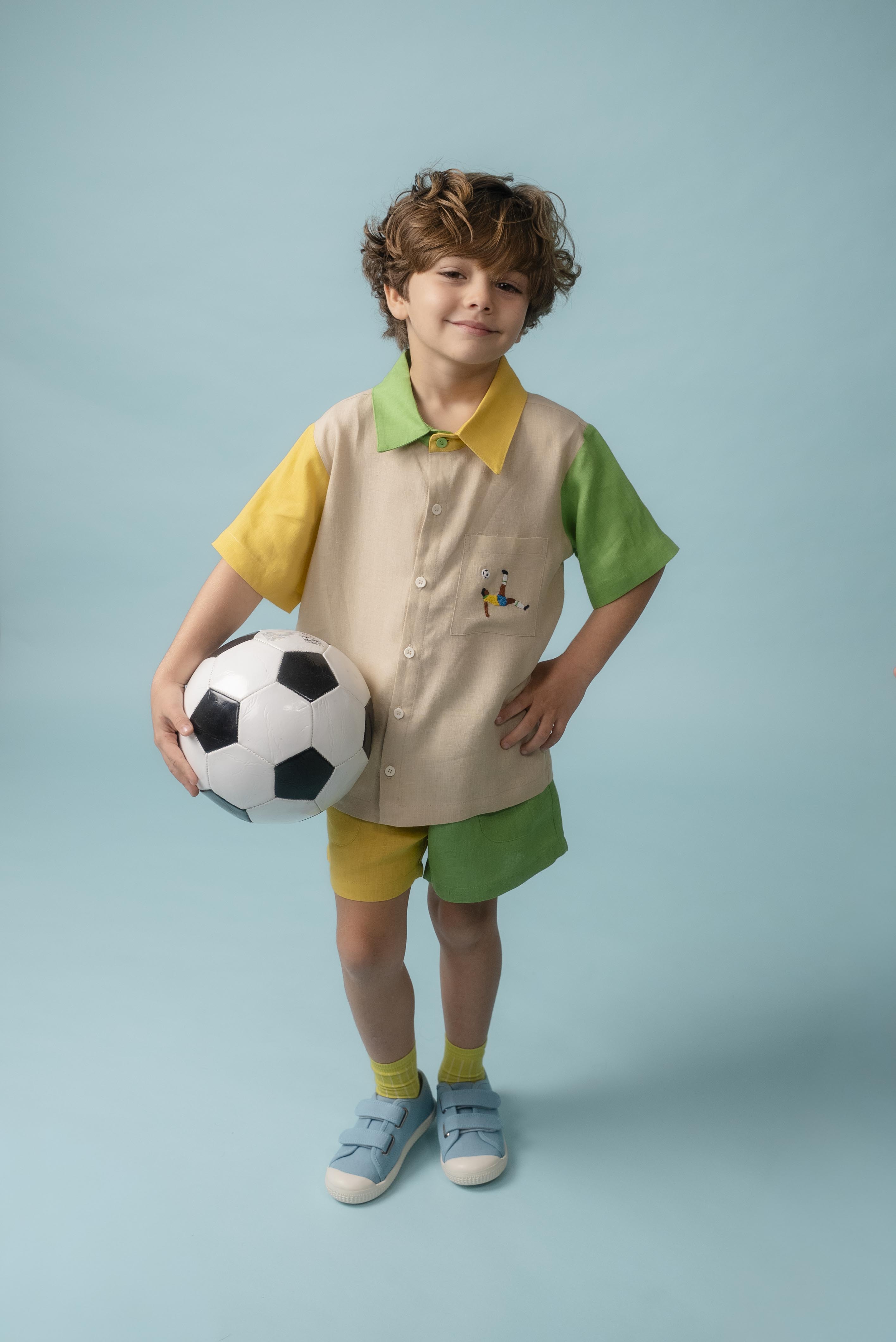Menino usando Camisa Tom em linho puro com bordado de jogador de futebol, combinada com shorts bicolor verde e amarelo