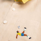 Detalhe do bordado à mão de jogador de futebol inspirado na bicicleta de Pelé em camisa infantil de linho puro