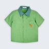 Camisa infantil Tom em linho verde com gola verde aspargo e cachorro caramelo bordado à mão no bolso frontal, vista de frente