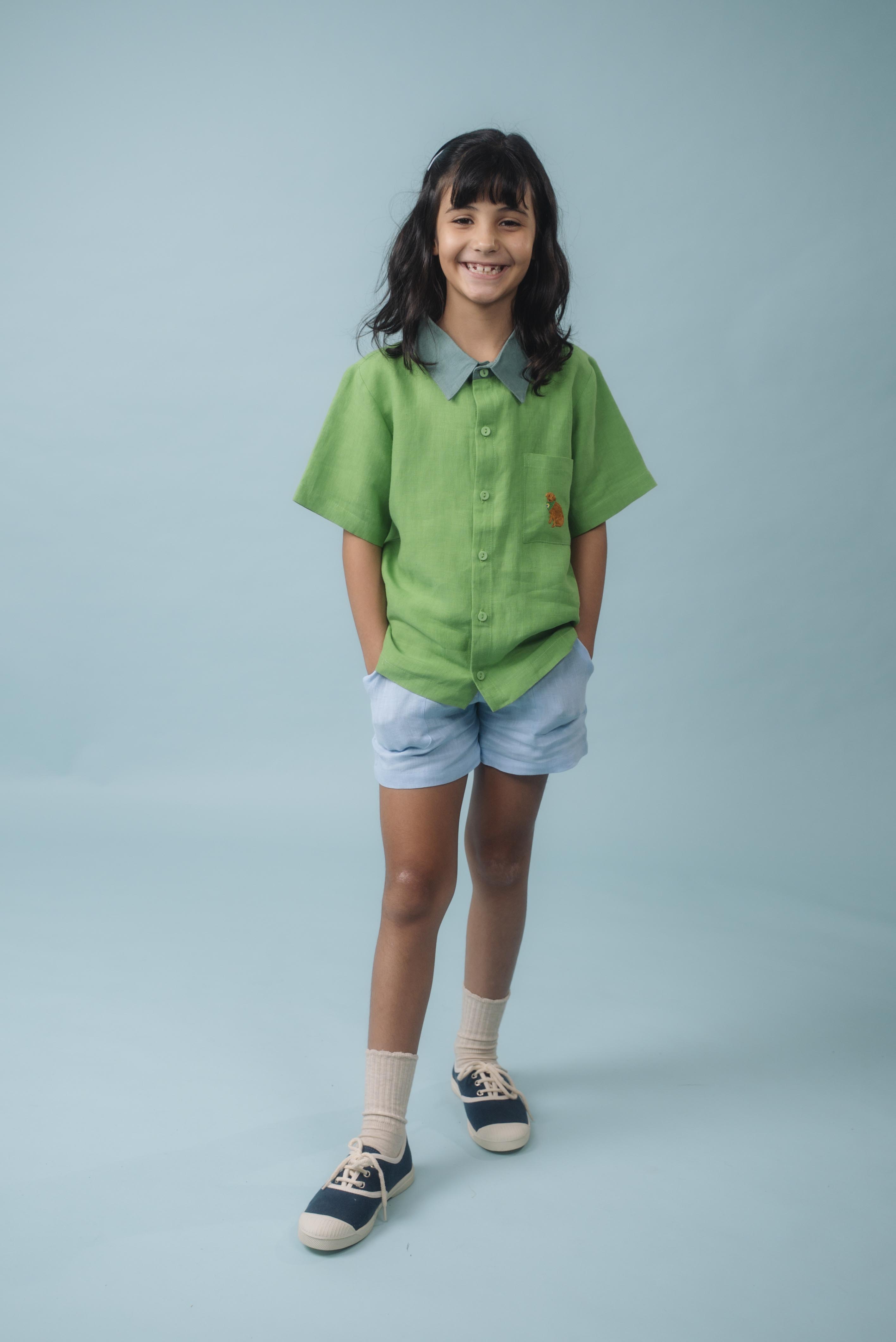 Menina usando Camisa Tom em linho verde com gola verde aspargo e bordado de cachorro caramelo no bolso