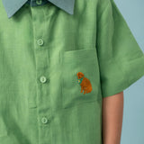 Menino usando camisa infantil verde em linho puro com gola verde aspargo e bordado à mão de cachorro caramelo