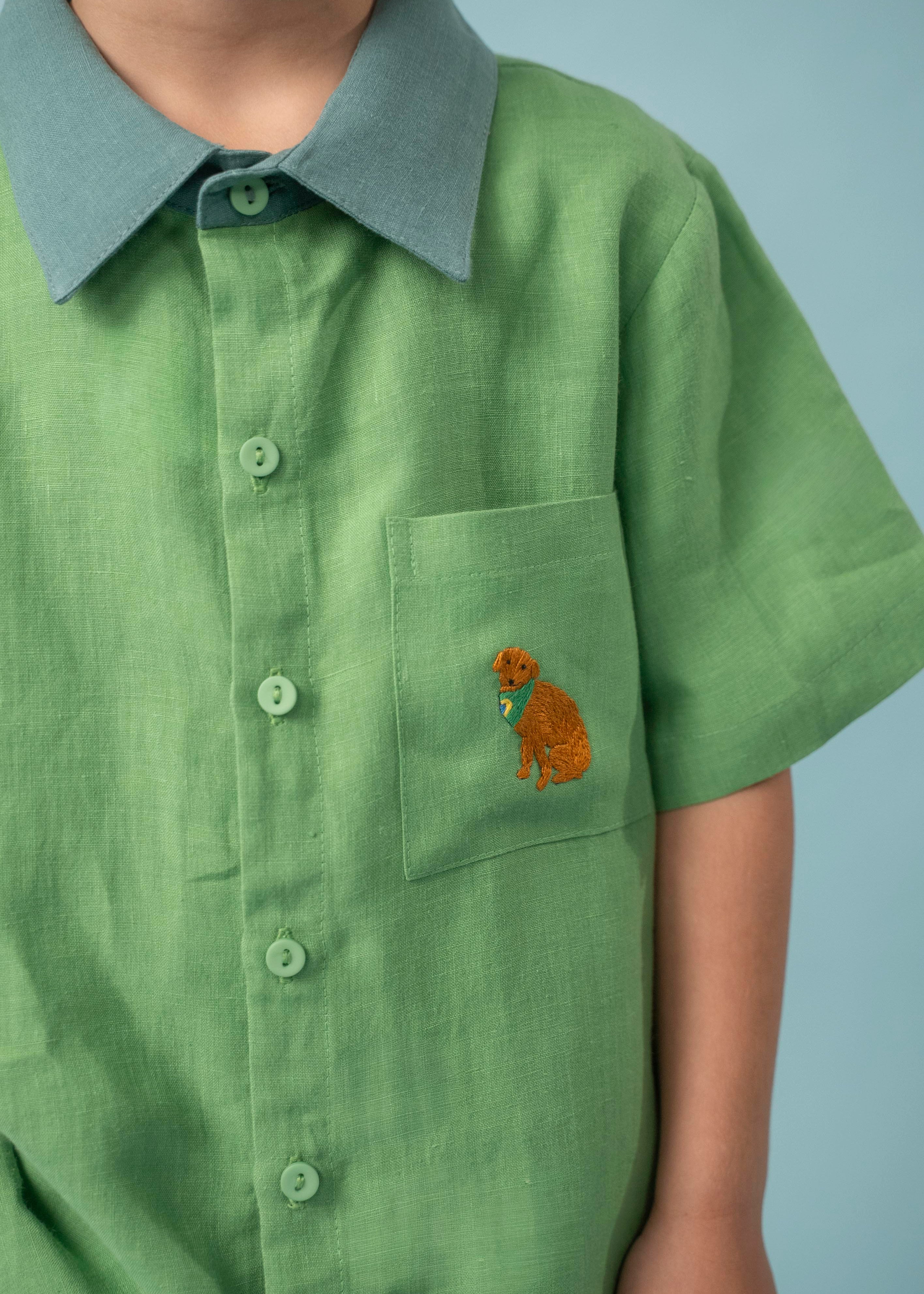 Menino usando camisa infantil verde em linho puro com gola verde aspargo e bordado à mão de cachorro caramelo