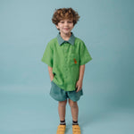 Menino usando Camisa Tom bicolor verde em linho puro com bordado de cachorro caramelo, combinada com shorts em mesmo tom da gola