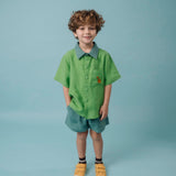 Menino usando Camisa Tom bicolor verde em linho puro com bordado de cachorro caramelo, combinada com shorts em mesmo tom da gola