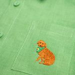 Detalhe do bordado à mão de cachorro caramelo no bolso de camisa infantil em linho puro verde