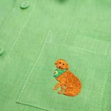 Detalhe do bordado à mão de cachorro caramelo no bolso de camisa infantil em linho puro verde