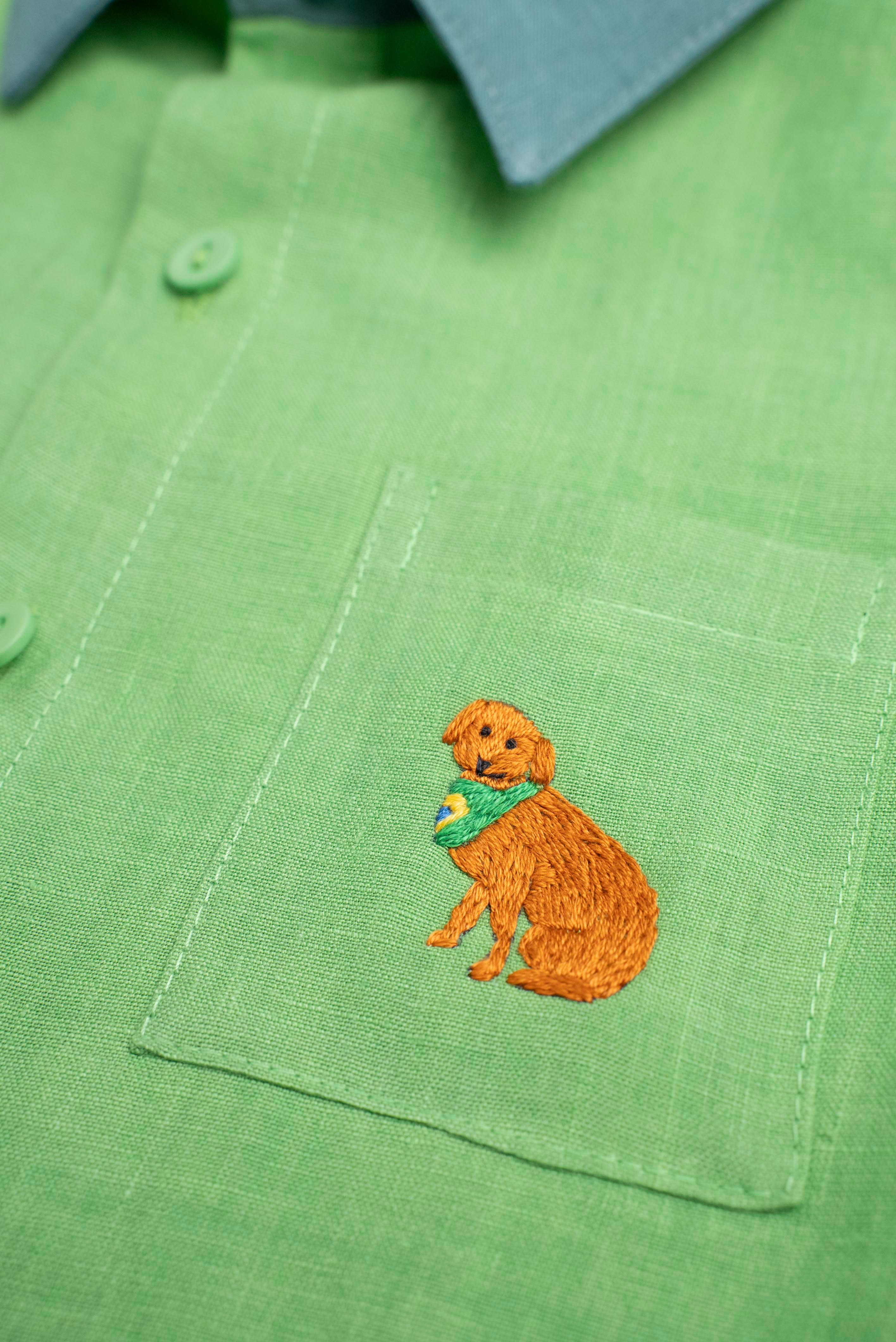 Detalhe do bordado à mão de cachorro caramelo no bolso de camisa infantil em linho puro verde