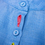 Close dos peixinhos bordados à mão entre os botões da Camisa Bento em linho azul fio tinto, com trama texturizada.