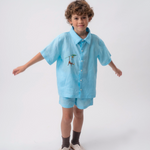 Menino usando conjunto azul turquesa com Camisa Tom em linho bordada à mão e shorts coordenado.