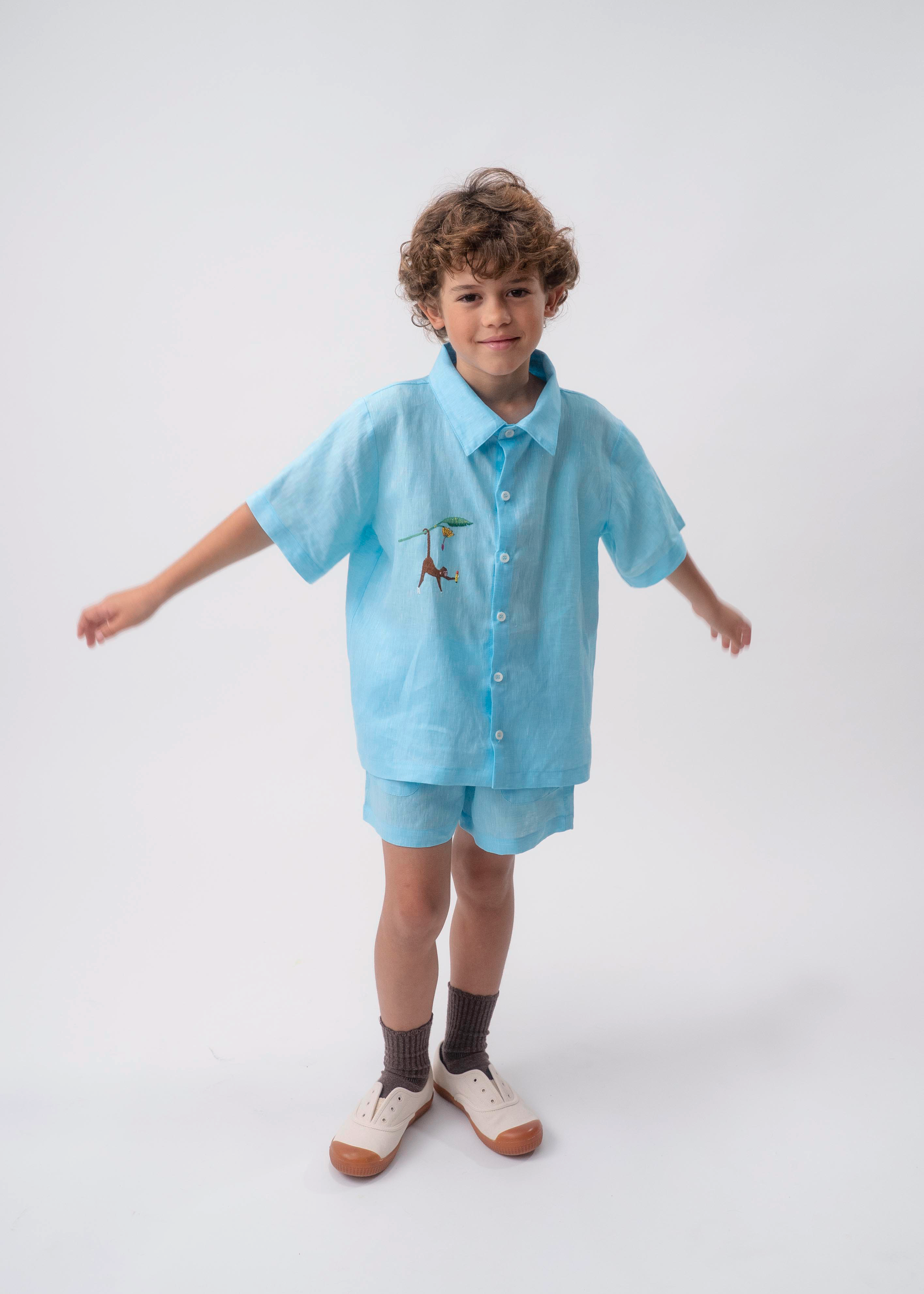 Menino usando conjunto azul turquesa com Camisa Tom em linho bordada à mão e shorts coordenado.