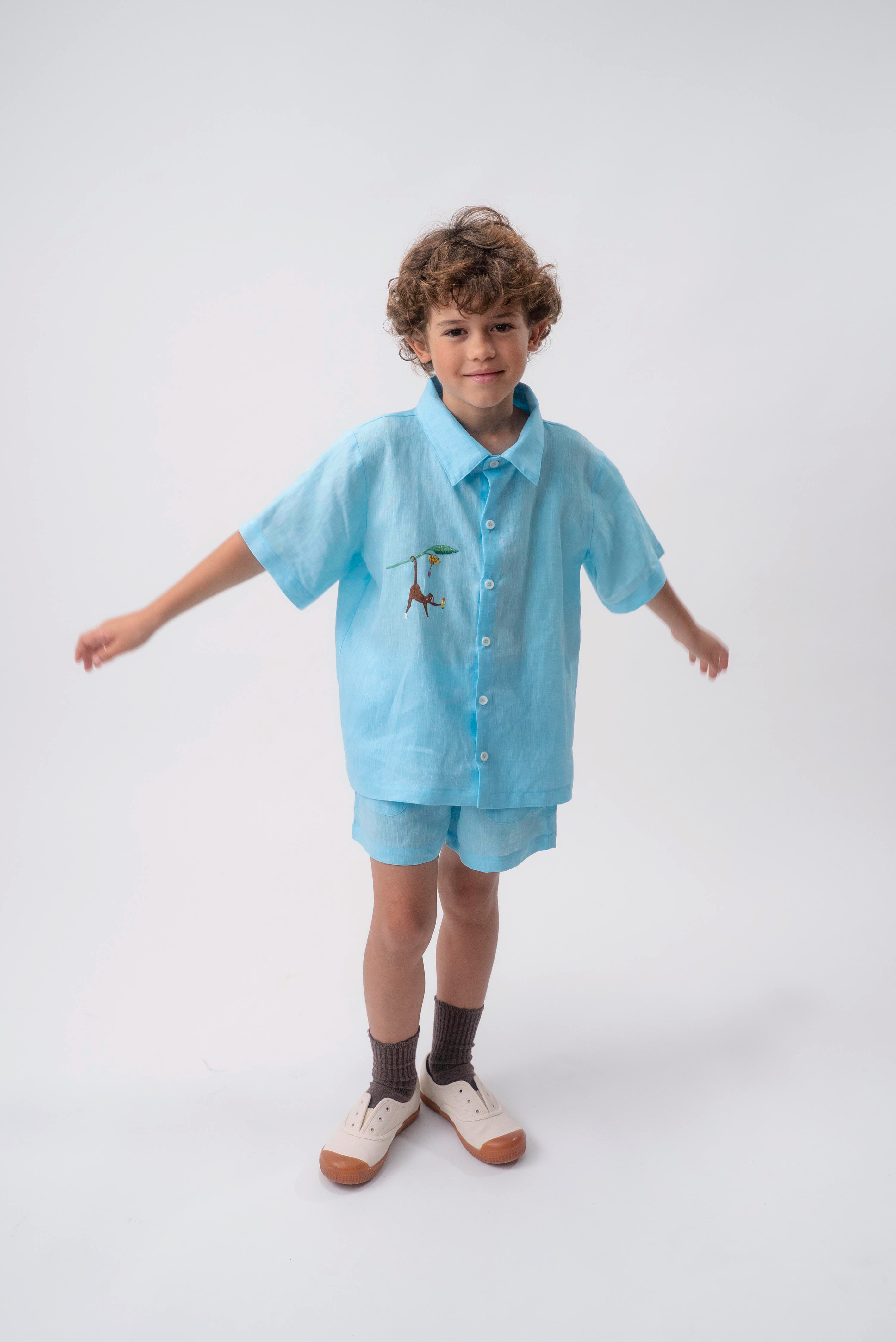 Menino usando conjunto azul turquesa com Camisa Tom em linho bordada à mão e shorts coordenado.