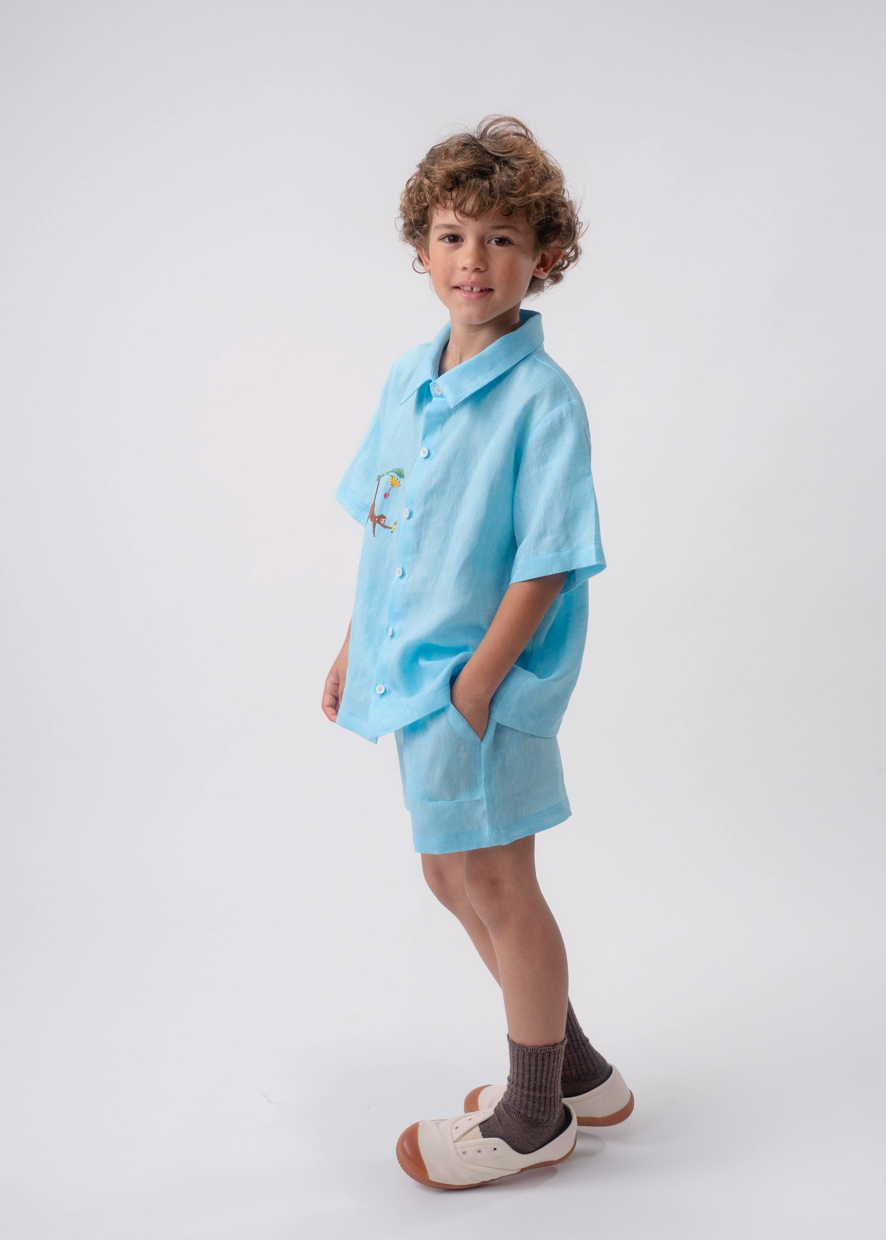 Menino usando Camisa Tom em linho azul turquesa com bordado de macaco e shorts coordenado.