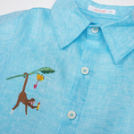 Detalhe da Camisa Tom infantil em linho azul turquesa com gola, botões claros e macaco bordado à mão.