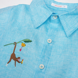 Detalhe da Camisa Tom infantil em linho azul turquesa com gola, botões claros e macaco bordado à mão.