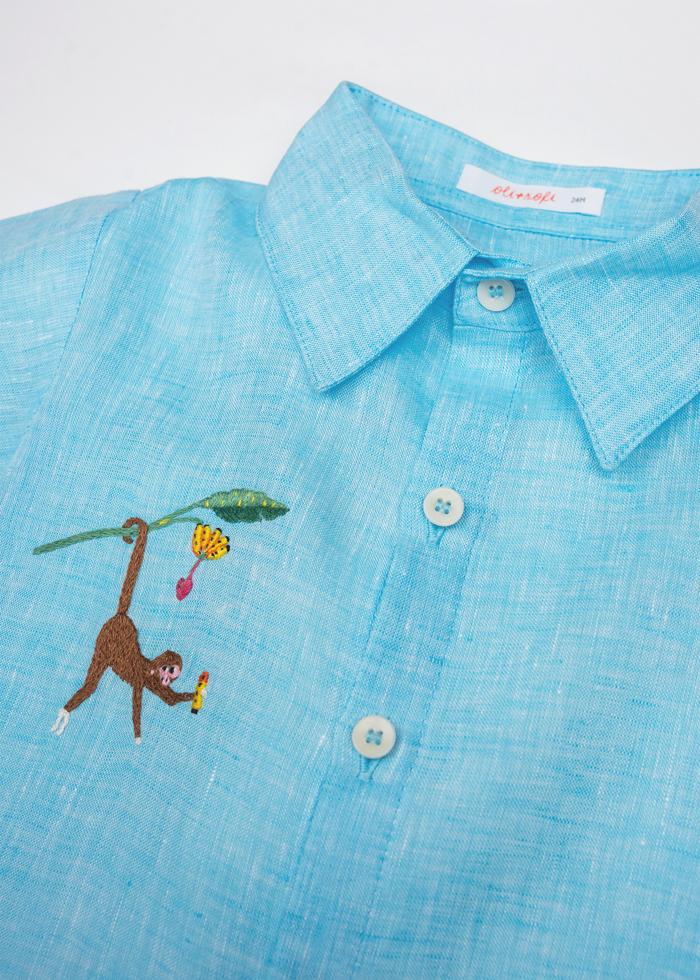 Detalhe da Camisa Tom infantil em linho azul turquesa com gola, botões claros e macaco bordado à mão.