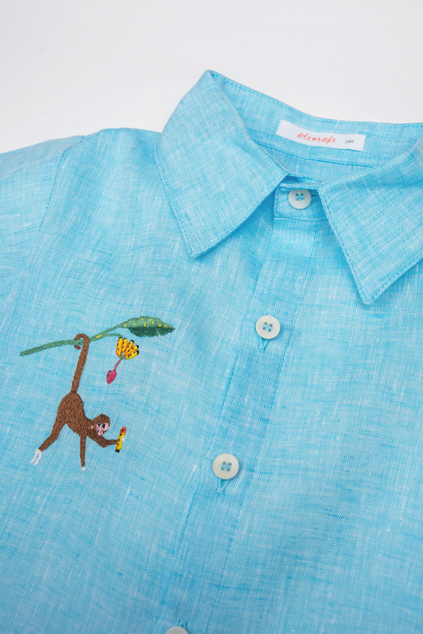 Detalhe da Camisa Tom infantil em linho azul turquesa com gola, botões claros e macaco bordado à mão.