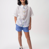 Menina usando Camisa Tom branca em linho com aves brasileiras bordadas à mão e shorts azul.