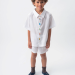 Menino usando Camisa Tom branca em 100% linho com aves brasileiras bordadas à mão e shorts branco.