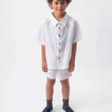 Menino usando Camisa Tom branca em 100% linho com aves brasileiras bordadas à mão e shorts branco.