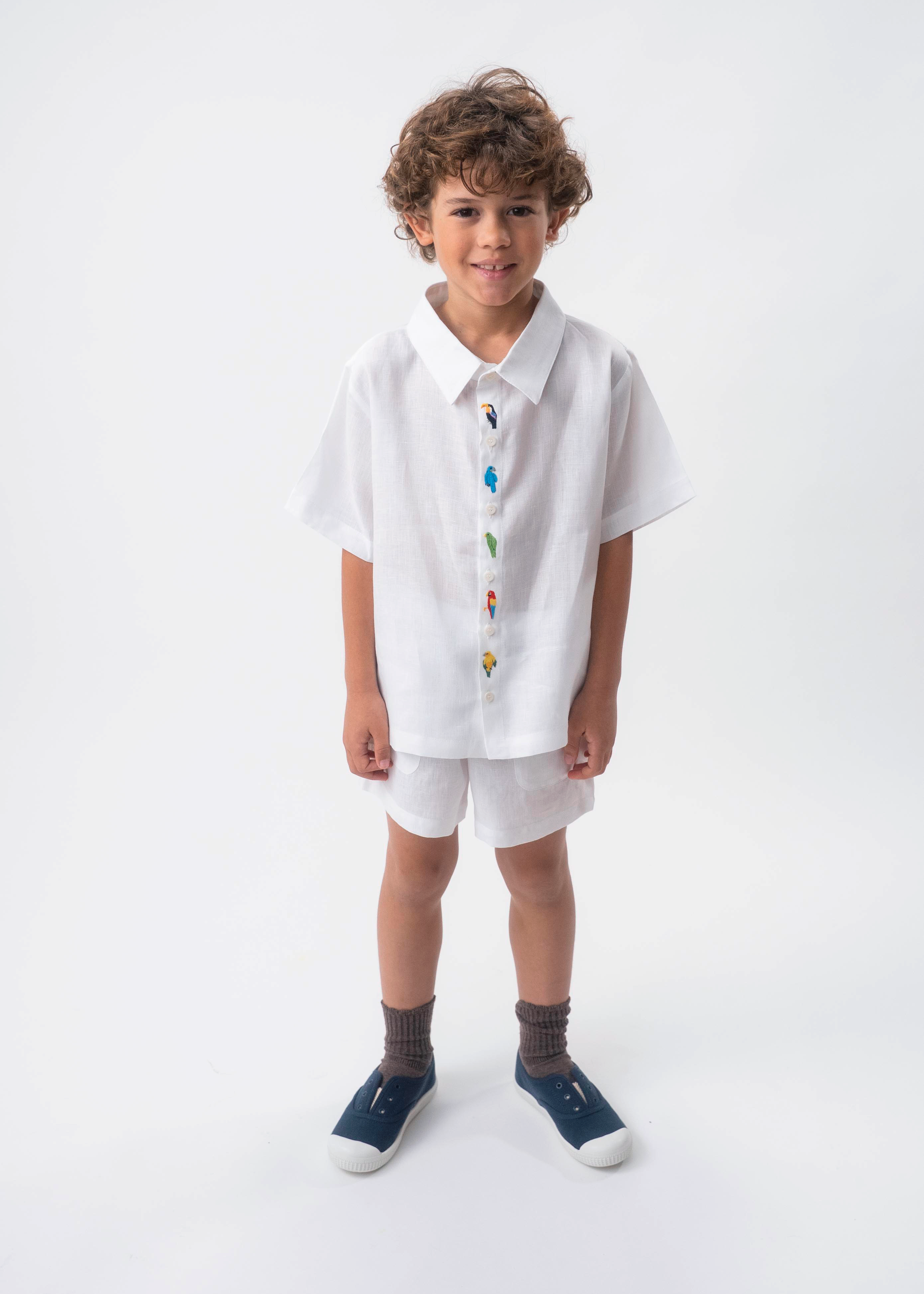 Menino usando Camisa Tom branca em 100% linho com aves brasileiras bordadas à mão e shorts branco.