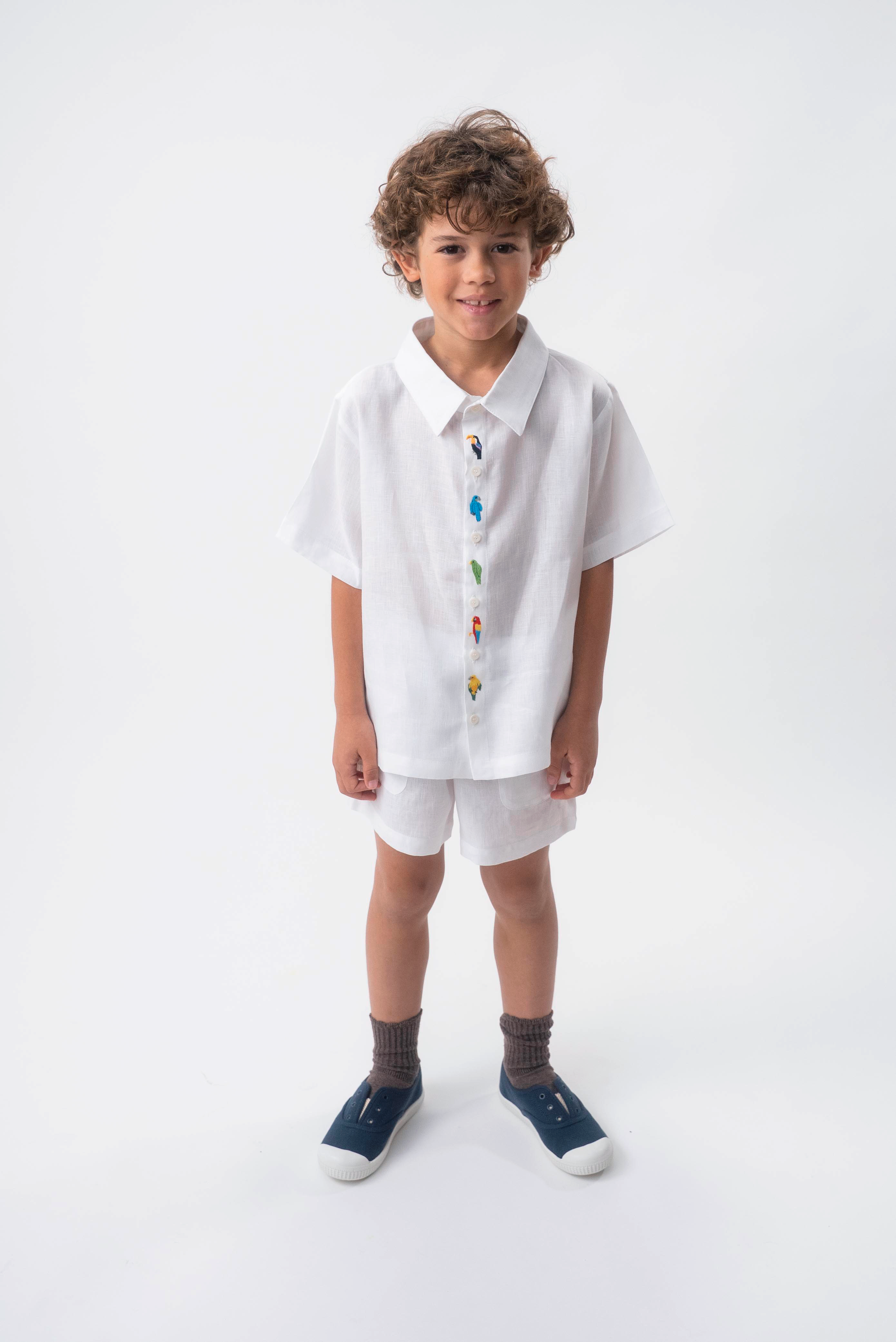 Menino usando Camisa Tom branca em 100% linho com aves brasileiras bordadas à mão e shorts branco.