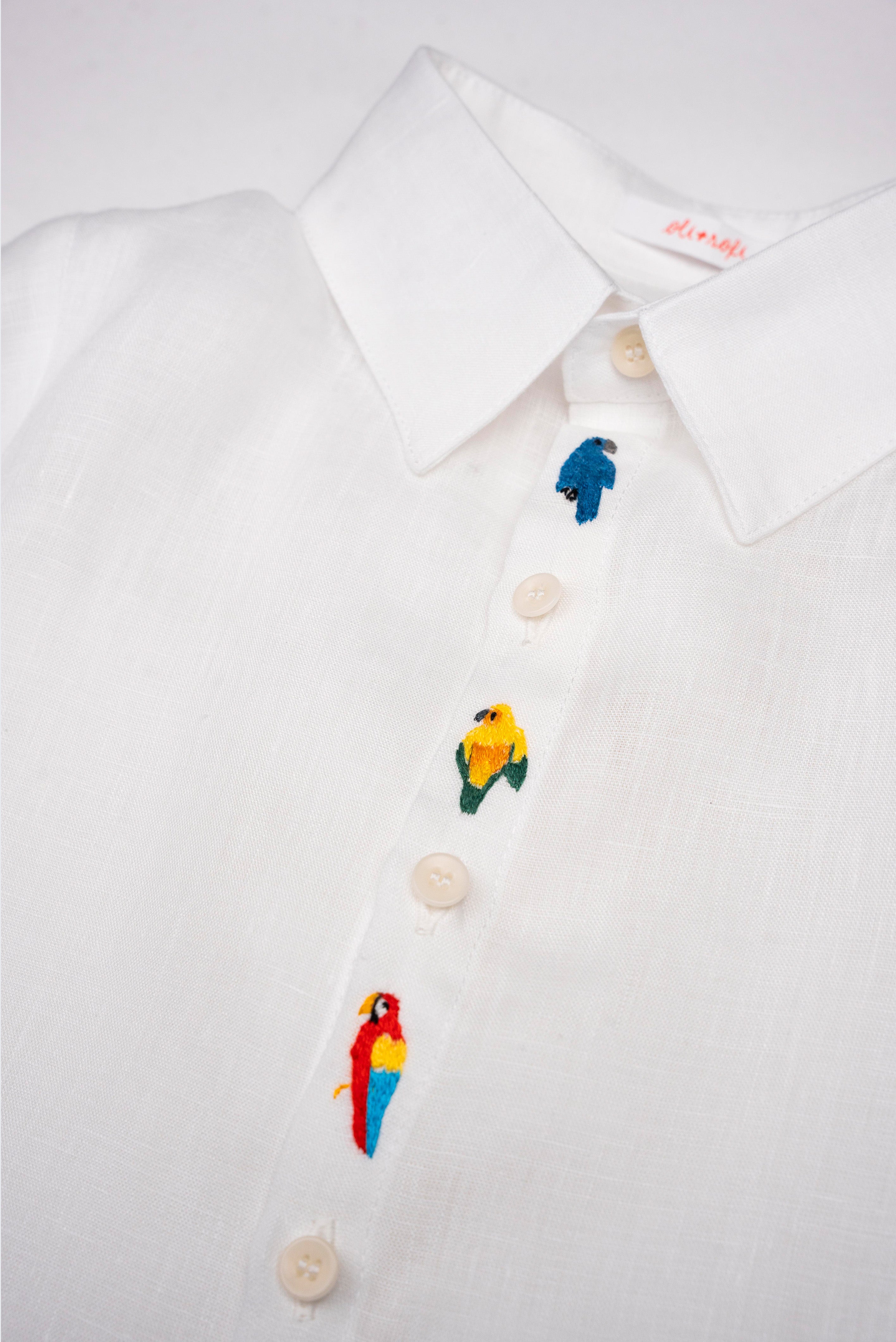 Detalhe da Camisa Tom infantil em linho branco com aves brasileiras bordadas à mão entre os botões.