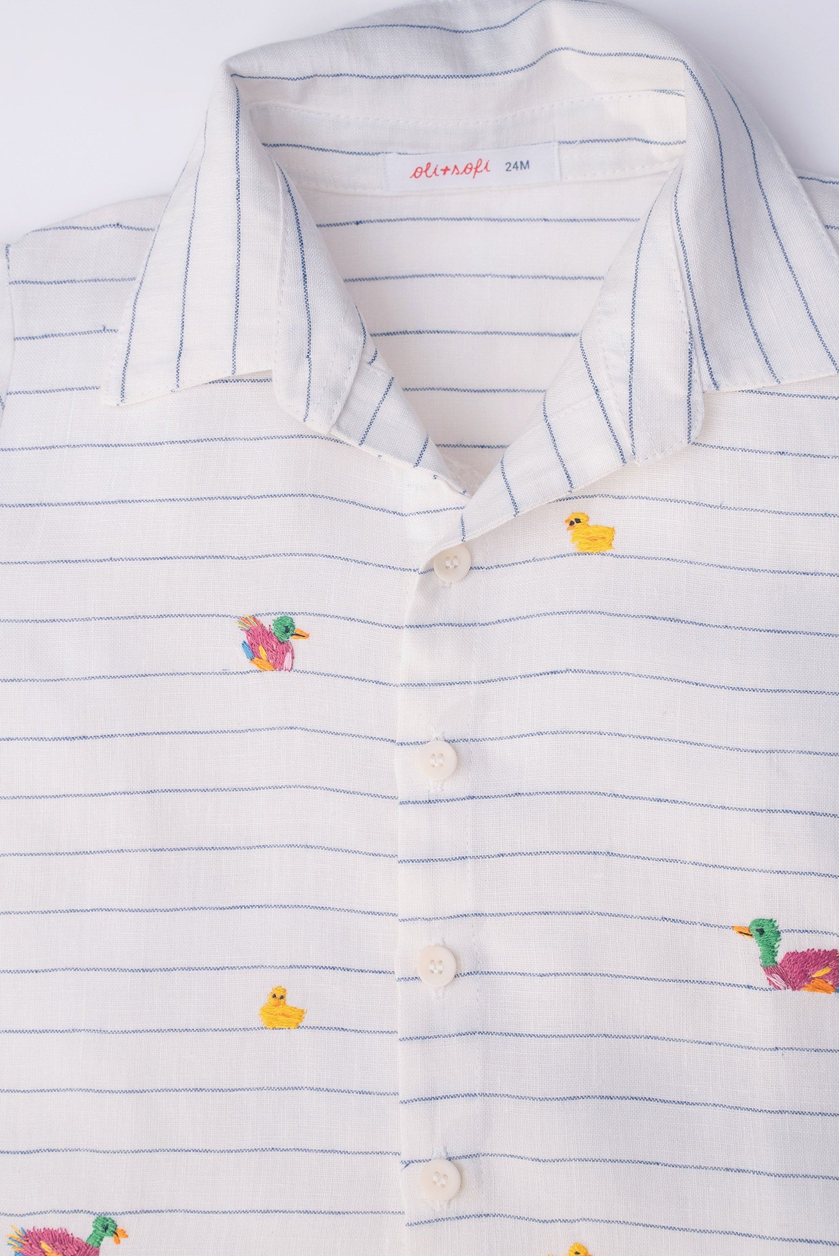 Camisa infantil listrada com patinhos bordados à mão com botões brancos, vista de frente em detalhe