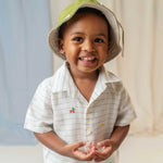 Menino usando camisa infantil listrada com patinhos bordados à mão e chapéu verde