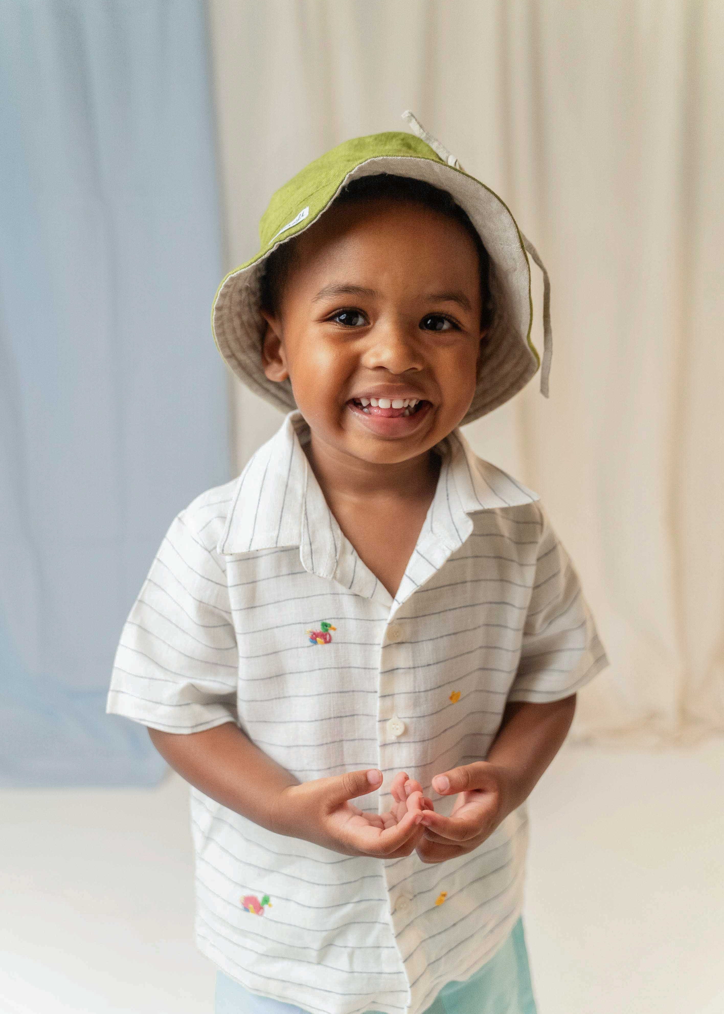 Menino usando camisa infantil listrada com patinhos bordados à mão e chapéu verde