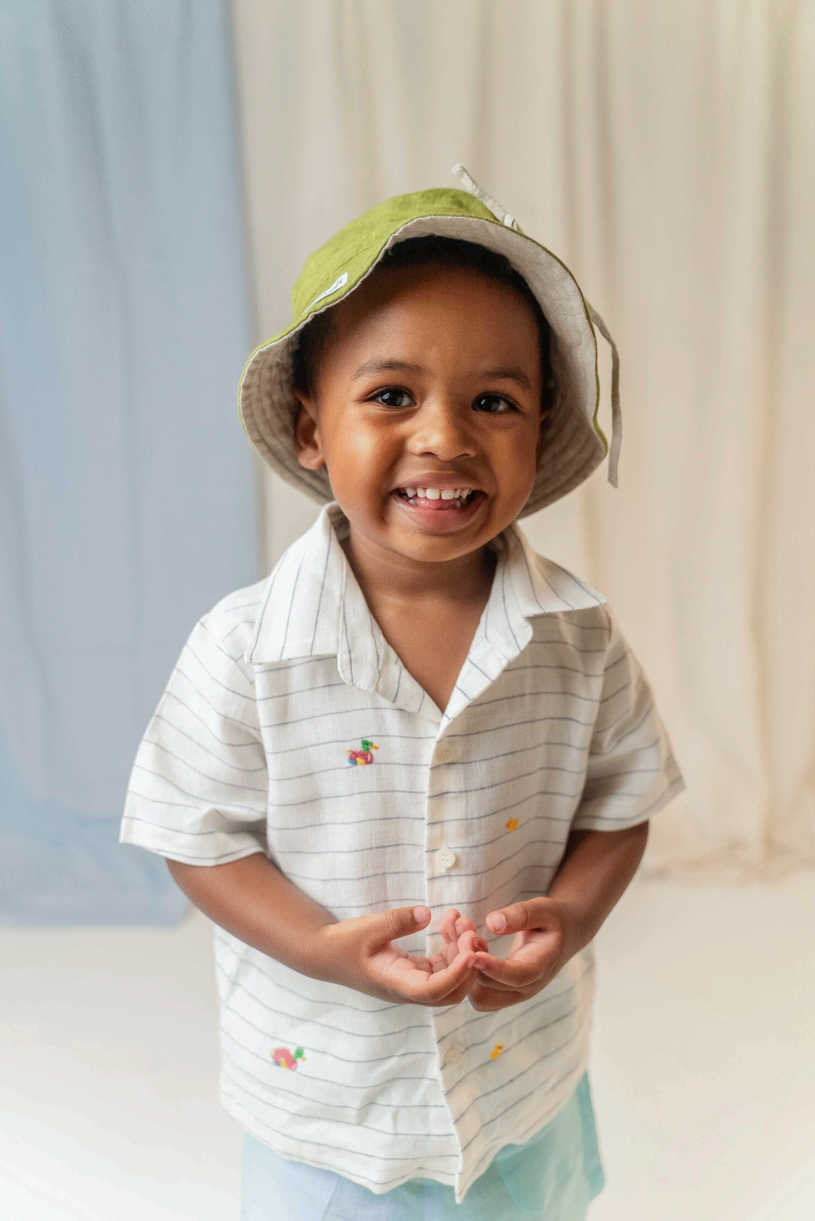 Menino usando camisa infantil listrada com patinhos bordados à mão e chapéu verde