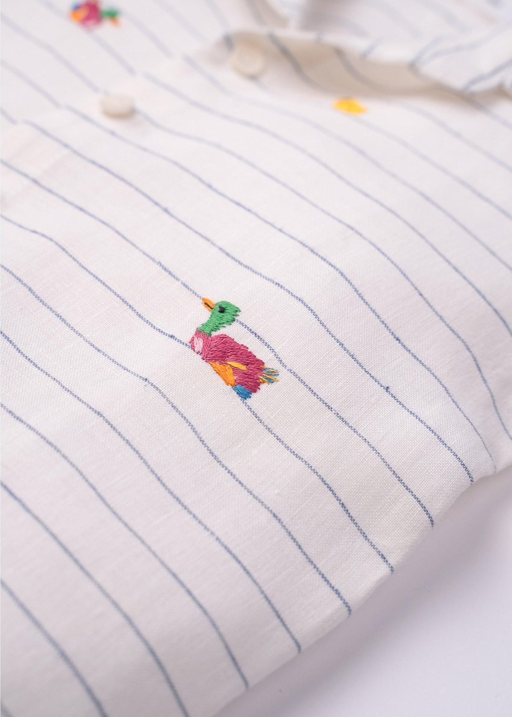 Detalhe do bordado artesanal de patinho colorido em camisa infantil listrada de linho claro
