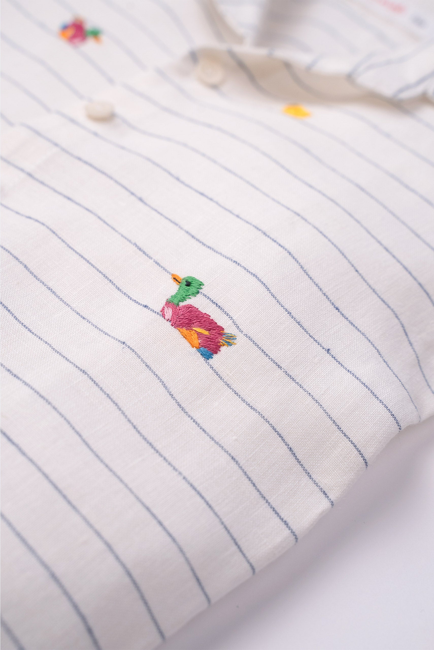 Detalhe do bordado artesanal de patinho colorido em camisa infantil listrada de linho claro