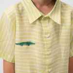 Detalhe da Camisa Tom em linho verde listrado vestida, com gola clássica, botões claros e jacaré bordado à mão.