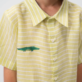 Detalhe da Camisa Tom em linho verde listrado vestida, com gola clássica, botões claros e jacaré bordado à mão.